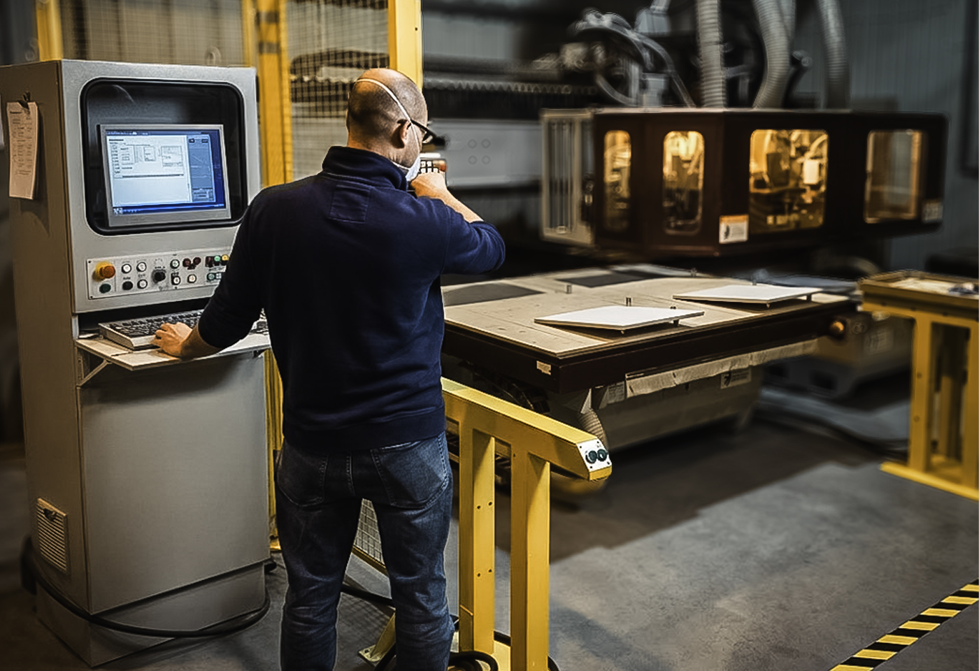 A Sarivale operator at the CNC control station, with cabinet panels on the machine bed behind.